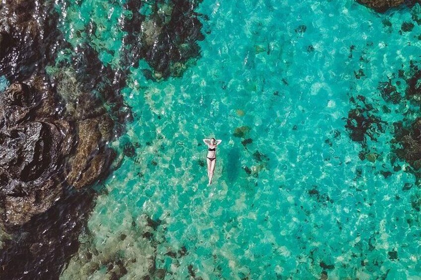 A person floating on a clear turquoise sea with rocky formations nearby. 3