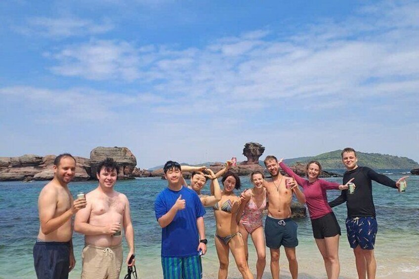 A group of people at a beach with clear water and rocky formations in the background. 5