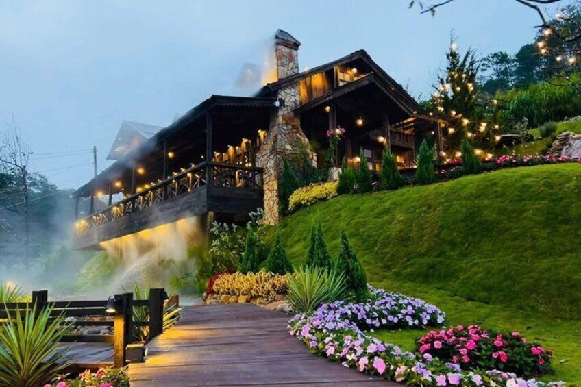 A lodge with a wooden deck, surrounded by colorful flowers and a well-maintained garden. 3