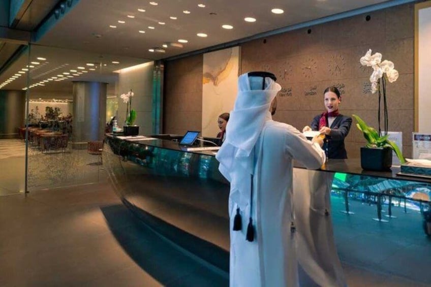 A modern hotel lobby with a reception desk, a receptionist, and a guest in traditional attire. 5