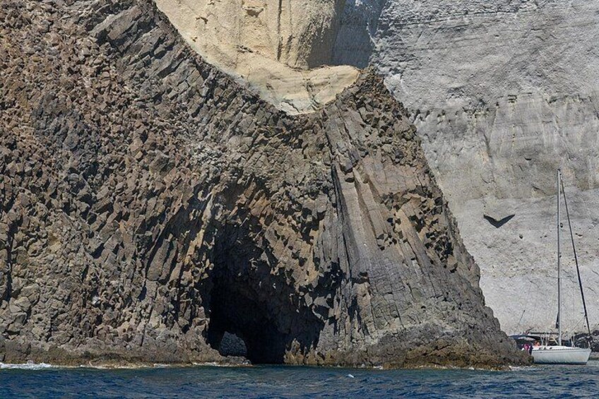 Un litorale roccioso con l'ingresso di una grotta, una barca a vela e un uccello in volo. 5