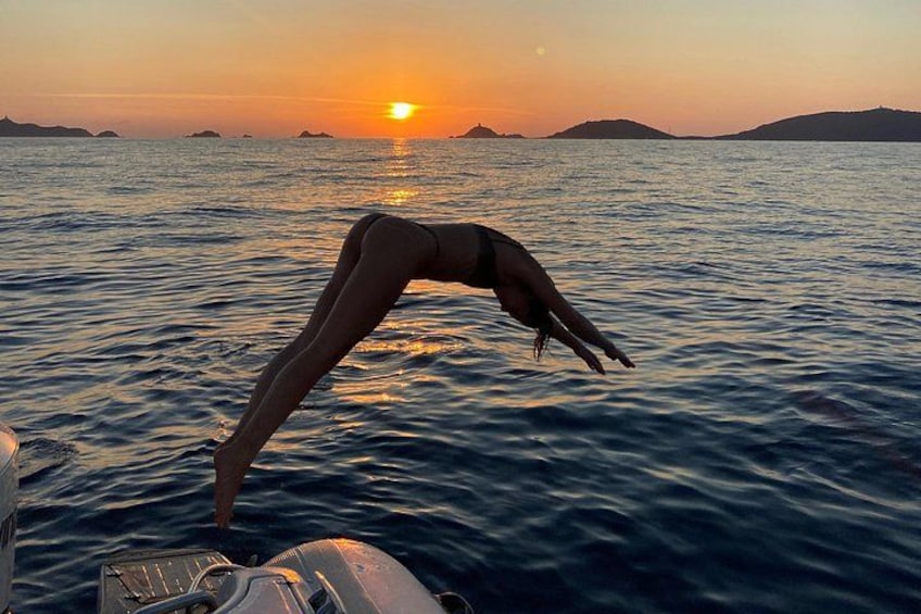 A person diving into the water at sunset with a boat in the foreground. 3