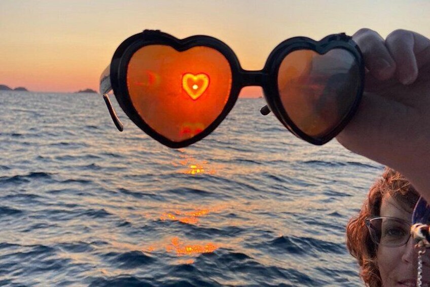 Heart-shaped sunglasses held up against a sunset over the ocean. 5