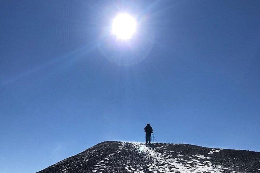 Eine Person steht auf einem mit Schnee bedeckten Hügel, im Hintergrund scheint die Sonne. 3