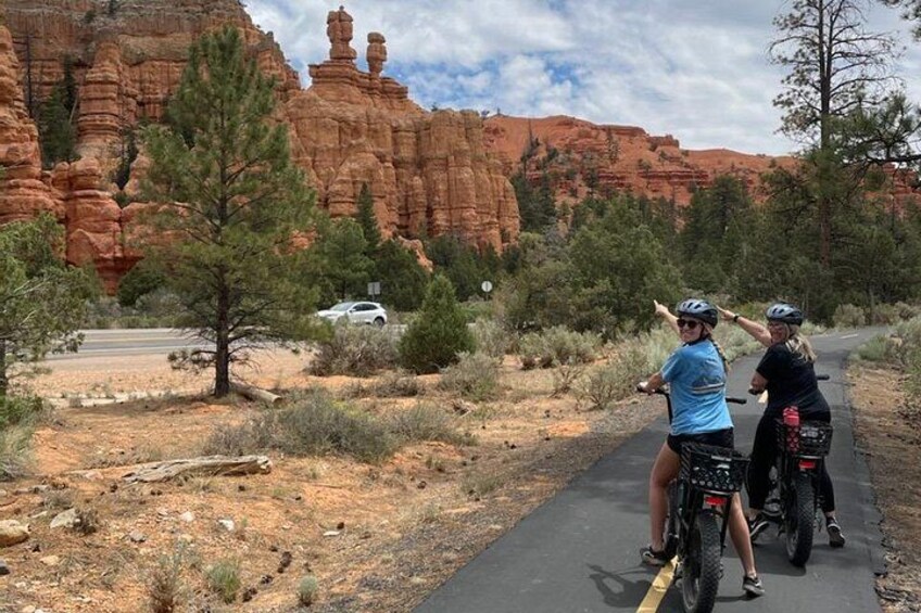 Deux personnes sur des vélos tout-terrain, sur un chemin pavé, avec des formations rocheuses rouges en arrière-plan. 2