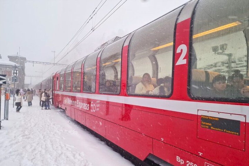 A red train with passengers, snow on the ground, and a sign indicating 'Bernina Express'. 4