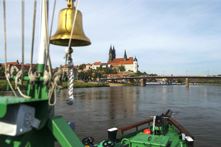 A green boat with a bell in the foreground, a river, and a castle with spires in the background. 4
