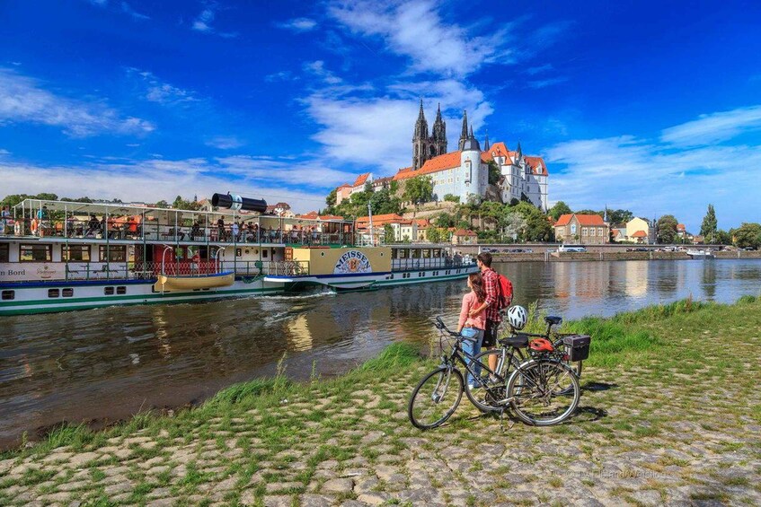 A river with boats, a castle, and a person with a bicycle. 3