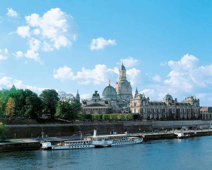 A river with a boat, a large historic building with domes, and trees along the riverbank. 1
