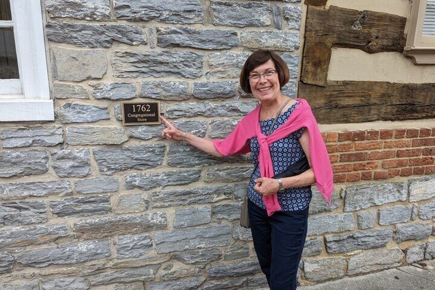 A person standing in front of a stone wall with a sign that reads "1762 Convivial Store." 3