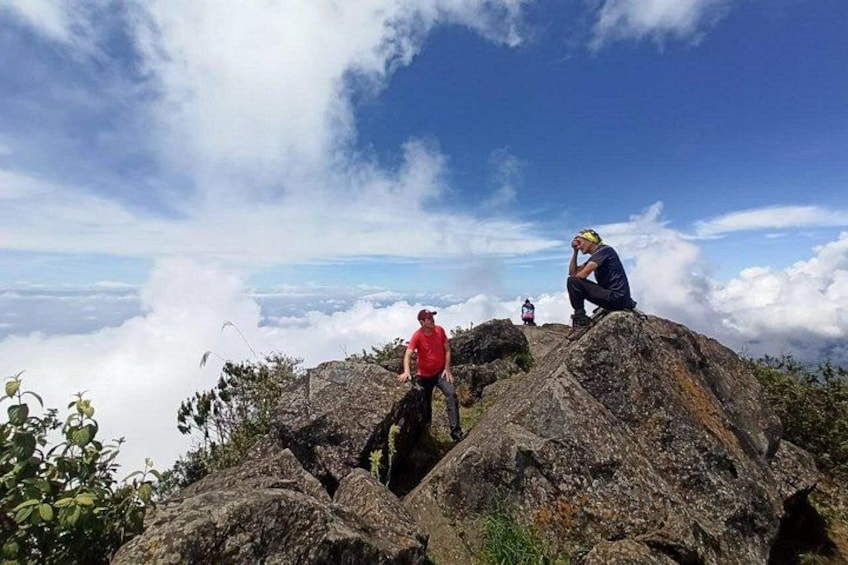 Trois personnes se tiennent au sommet d’une montagne rocheuse, d’où elles peuvent admirer les nuages en contrebas. 5