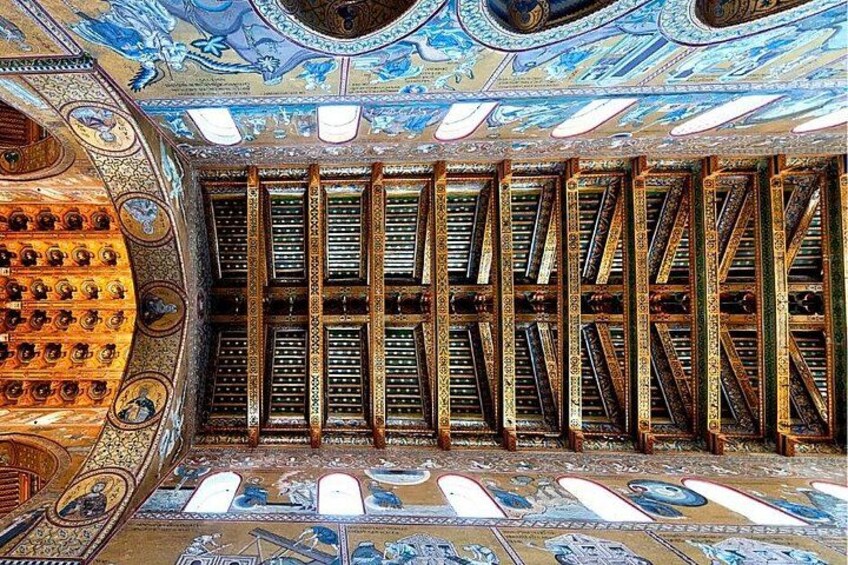 An ornate interior with intricate ceiling artwork, a patterned floor, and a series of wooden beams. 5