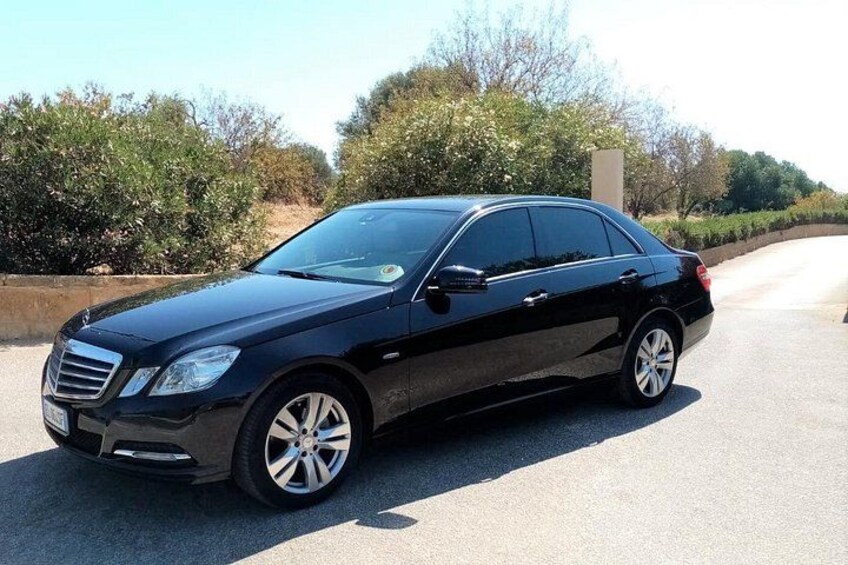 A black sedan parked on a road with trees and a clear sky in the background. 4