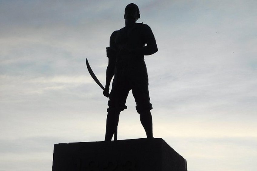 A silhouette of a person holding a sword on a pedestal against a cloudy sky. 1