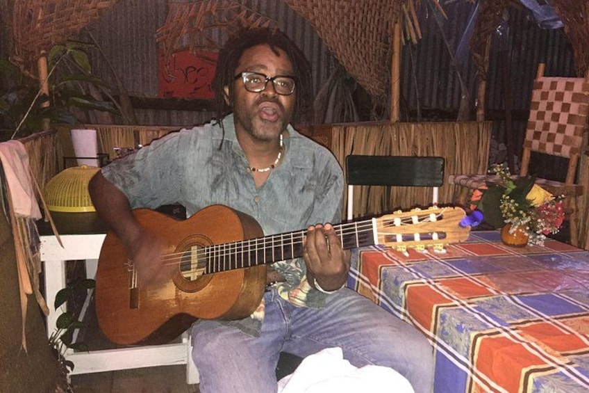 A person playing a guitar in a rustic setting with a checkered tablecloth and a woven chair. 3