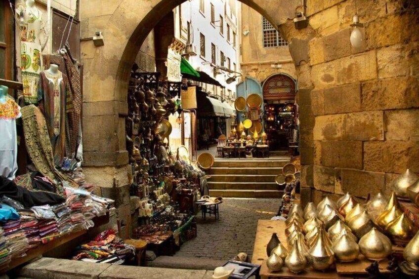 Une rue étroite bordée de boutiques des deux côtés, où sont exposés divers articles, notamment des vêtements et des objets en métal. 2