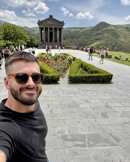 Mies ottaa selfien historiallisessa paikassa, taustalla näkyy temppeli ja edessä maisemoitu puutarha. 1