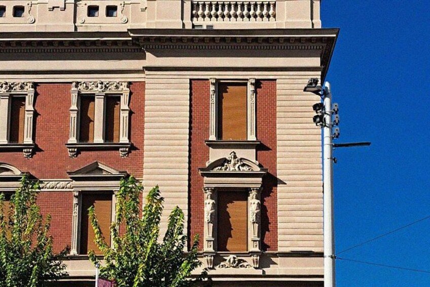 A multi-story building with red brick and beige siding, large windows, and decorative architectural details. 3