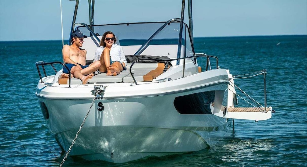 A small white motorboat with two people on board, anchored in calm waters. 3