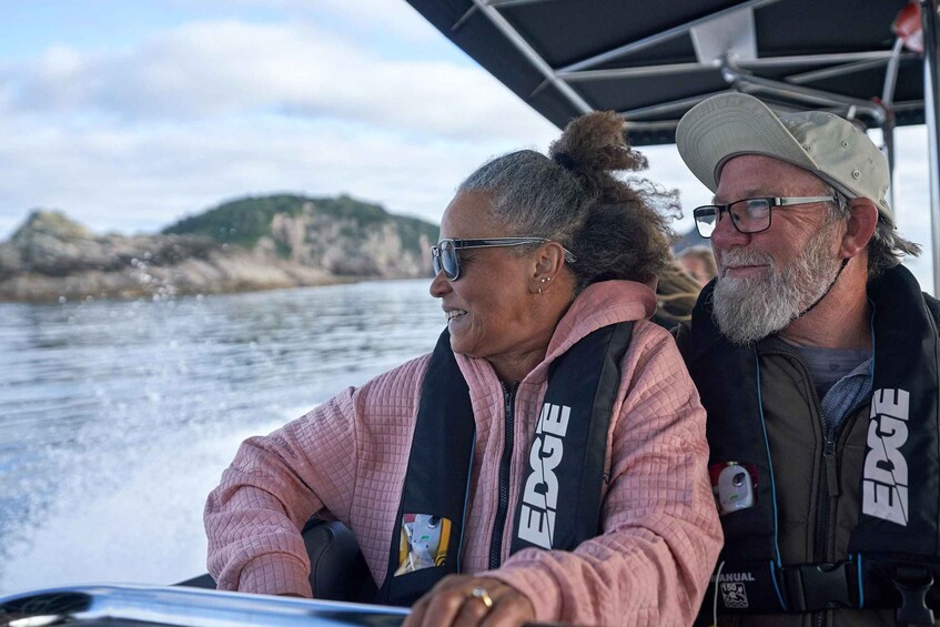 Two people on a boat with a rocky shoreline in the background. 5