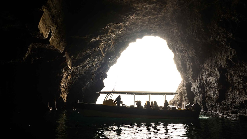 A boat with people inside, silhouetted against a bright light from a cave opening. 5