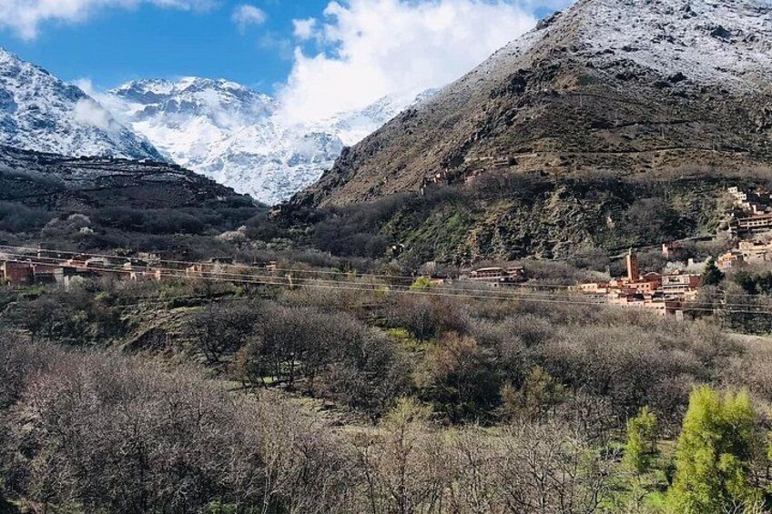 A mountainous landscape with snow-capped peaks, a valley with sparse vegetation, and a small settlement with buildings. 5