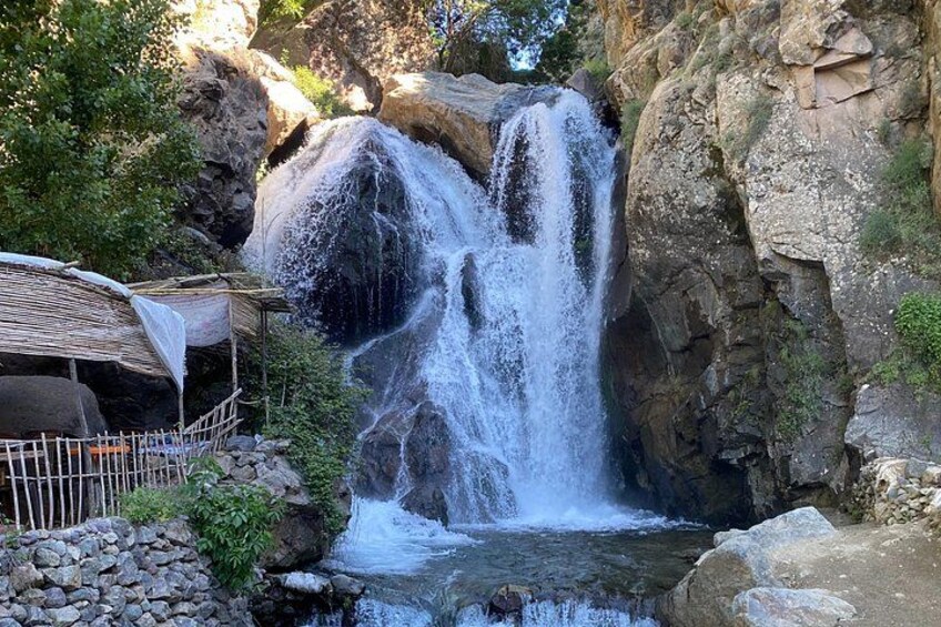 A waterfall cascading over rocks, a small stream, and a bamboo structure. 4