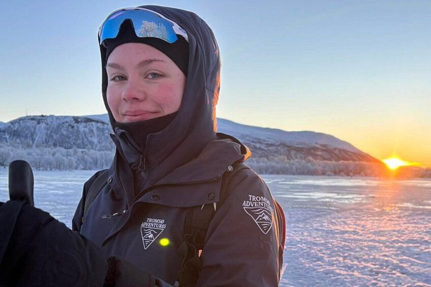 Una persona con abbigliamento invernale e un logo sulla giacca, in piedi su uno specchio d'acqua ghiacciato con un tramonto sullo sfondo. 3