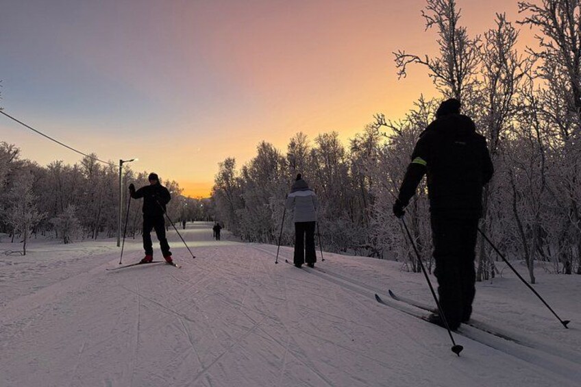 A cross-country skier on a snowy trail with trees and a sunset in the background. 2