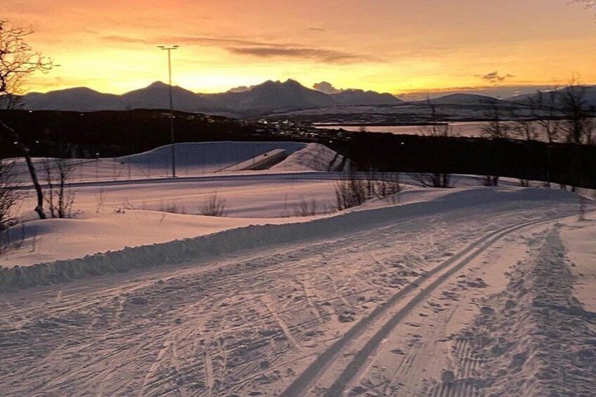 Paesaggio innevato con una pista da sci, montagne e un tramonto. 2