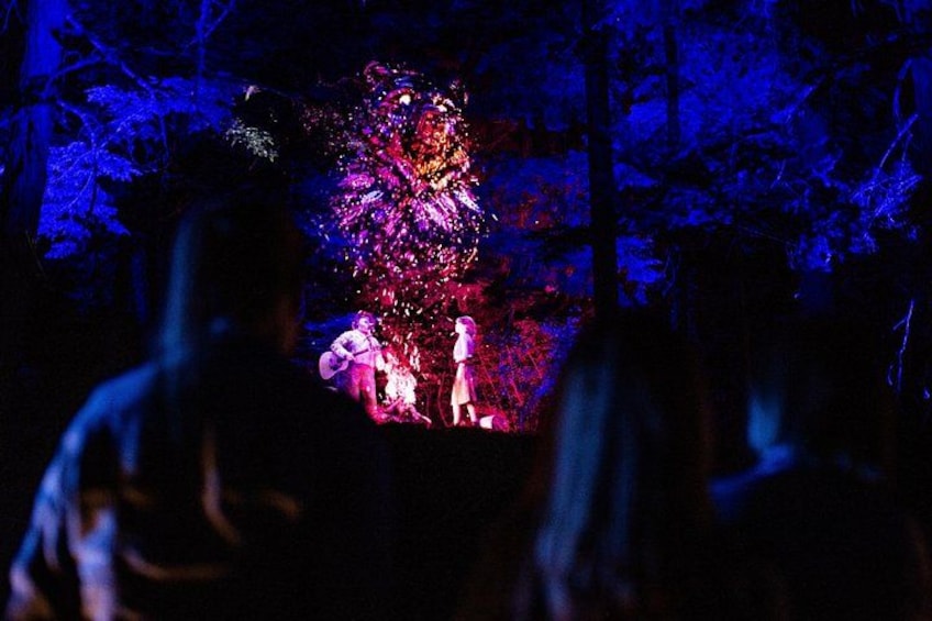 Een boslandschap met een fel verlichte boom en silhouetten van mensen. 3