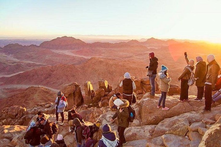 A group of people hiking on a rocky mountain trail during sunset. 1