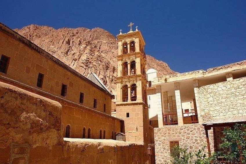 A historic building with a bell tower, stone walls, and a mountainous backdrop. 5