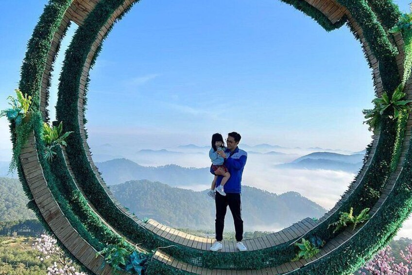 A couple standing on a circular wooden platform surrounded by greenery, overlooking a mountainous landscape. 5