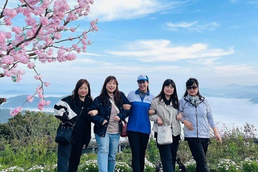 A group of people standing on a hill with cherry blossoms and a mountainous landscape in the background. 4