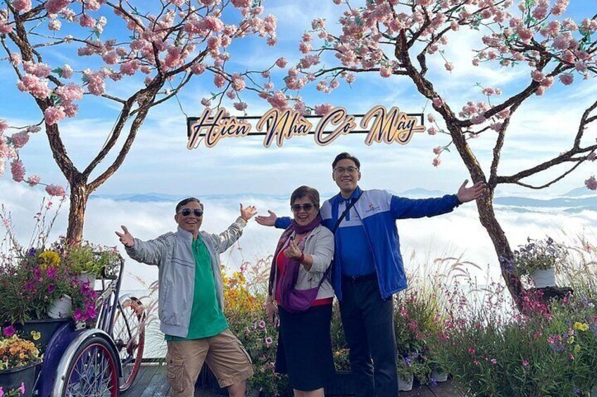 Three people standing in front of blooming cherry trees with a mountainous landscape in the background. 3