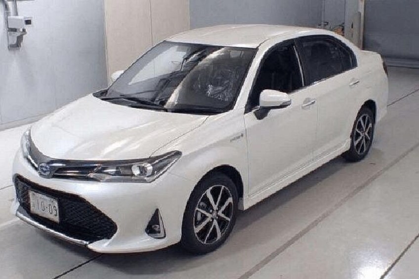 A white sedan parked indoors with a visible license plate, side mirrors, and alloy wheels. 1