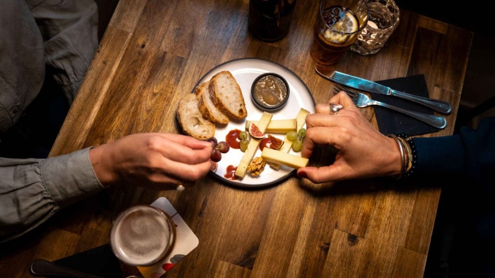 A wooden table with a plate of cheese, grapes, and nuts, a glass of beer, and a glass of iced tea. 2