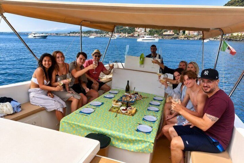A group of people on a boat with a table set for a meal, surrounded by water and a coastline. 2
