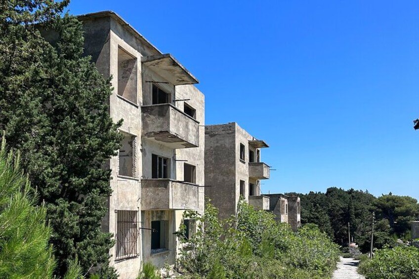 A multi-story building with balconies, surrounded by greenery and trees. 1