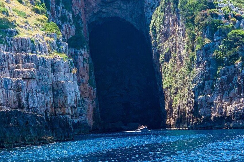 Eingang einer Küstenhöhle mit felsigen Klippen und einem Boot im Wasser. 5