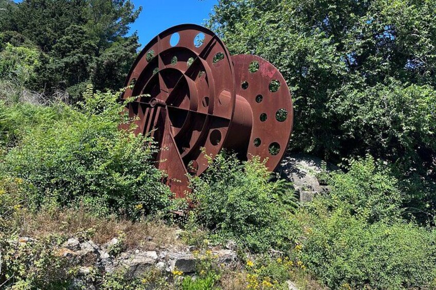 Eine große, verrostete Metallkonstruktion mit kreisförmigen Ausschnitten, umgeben von dichtem Grün und Bäumen. 2