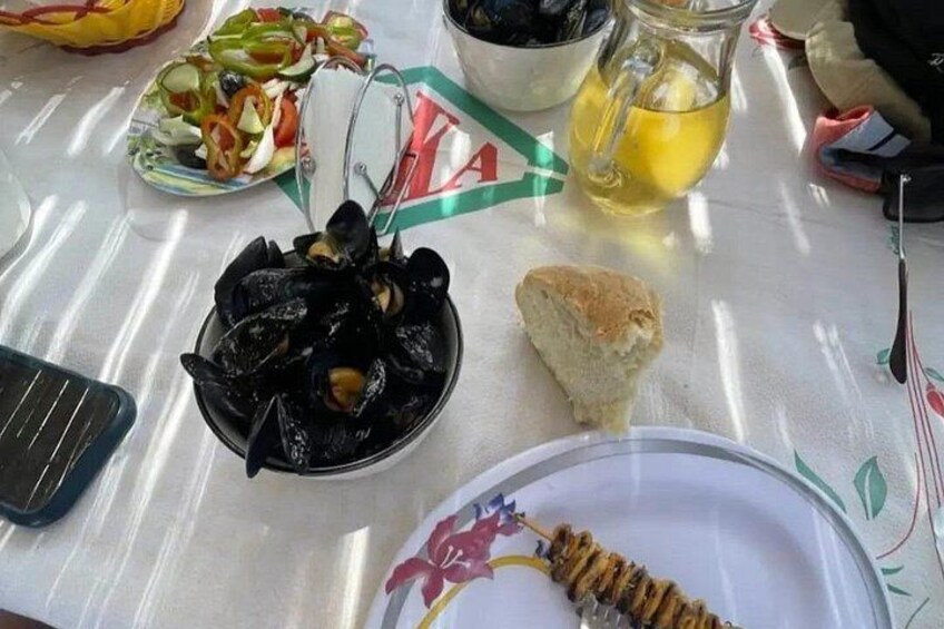 Et bord med en tallerken fyldt med muslinger, en citronkande, en sandwich og en salat. 5