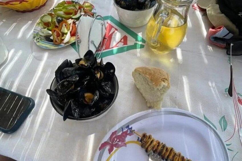 Et bord med en tallerken fyldt med muslinger, et brød og et kander med citronsaft. 1
