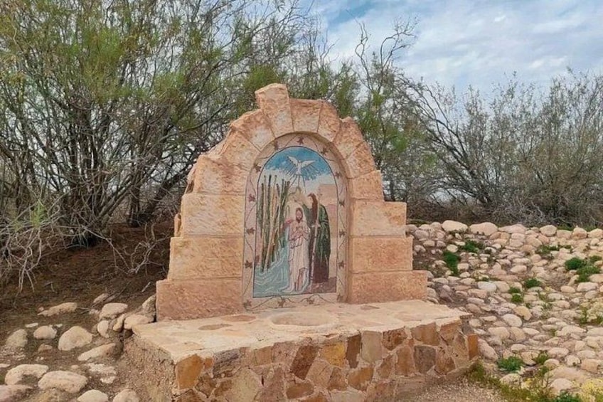A stone monument with a relief sculpture depicting figures, surrounded by desert vegetation and rocks. 3