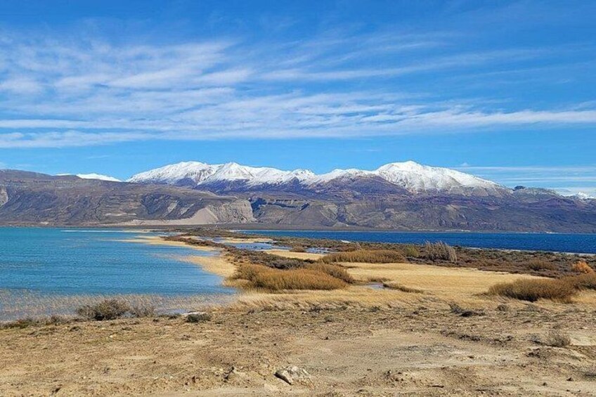 A lake with mountains in the background, a sandy beach, and dry grassland. 2