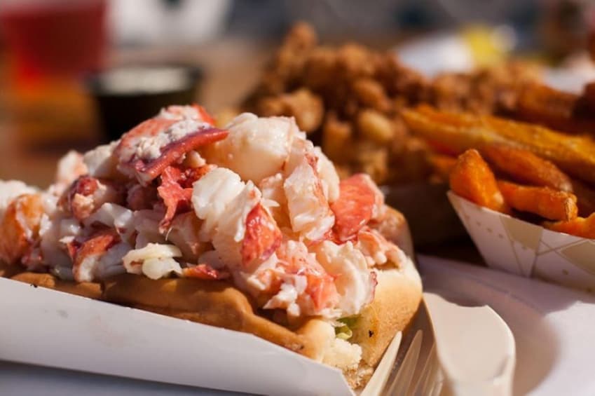 En lobster sandwich med pommes frites og en drik i baggrunden. 3