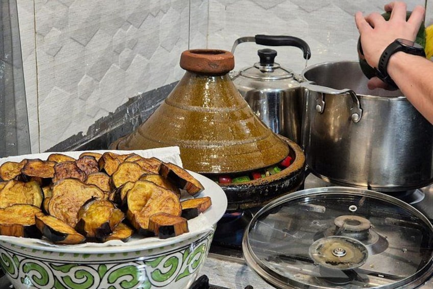 A traditional Moroccan tagine, a large clay pot, and a metal pot on a stove. 2