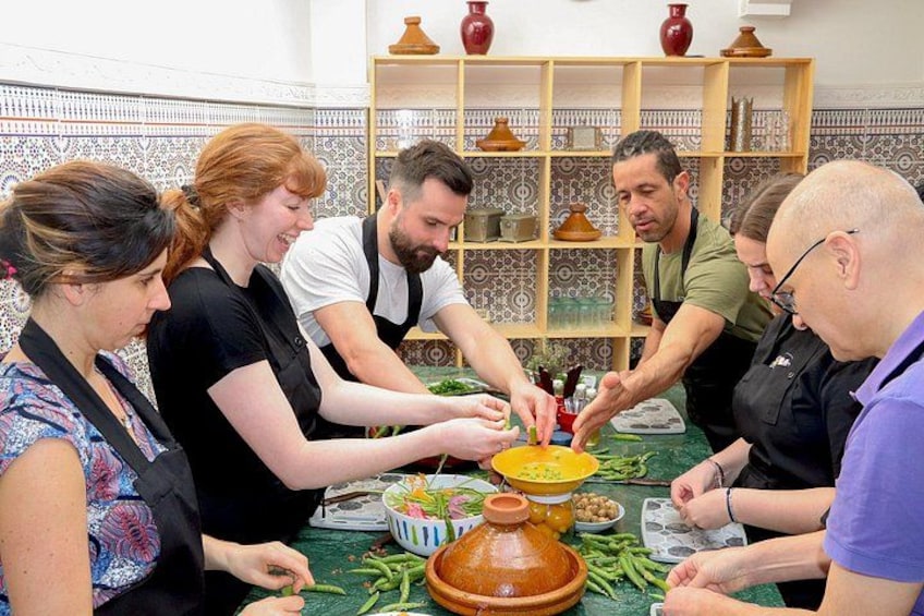 A group of people preparing food around a table with a large clay pot and vegetables. 5