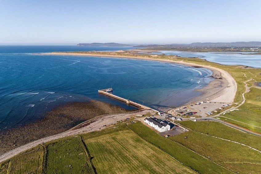Oversigtsbillede af et kystområde med en mole, der strækker sig ud i havet, en sandstrand og en lille bebyggelse med huse. 2
